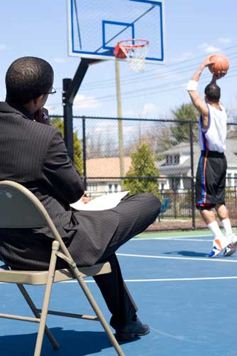 An athlete agent watches a client play basketball.