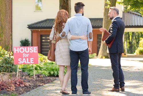 A couple looks at a house with a 'for sale' sign