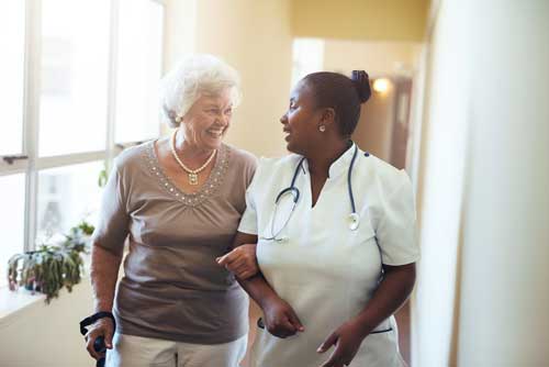 A nursing home resident walks with a care taker.